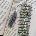 A decorative bookmark made of multiple small illustrated book spines arranged vertically, with a gray tassel and silver string, placed on an open book page.