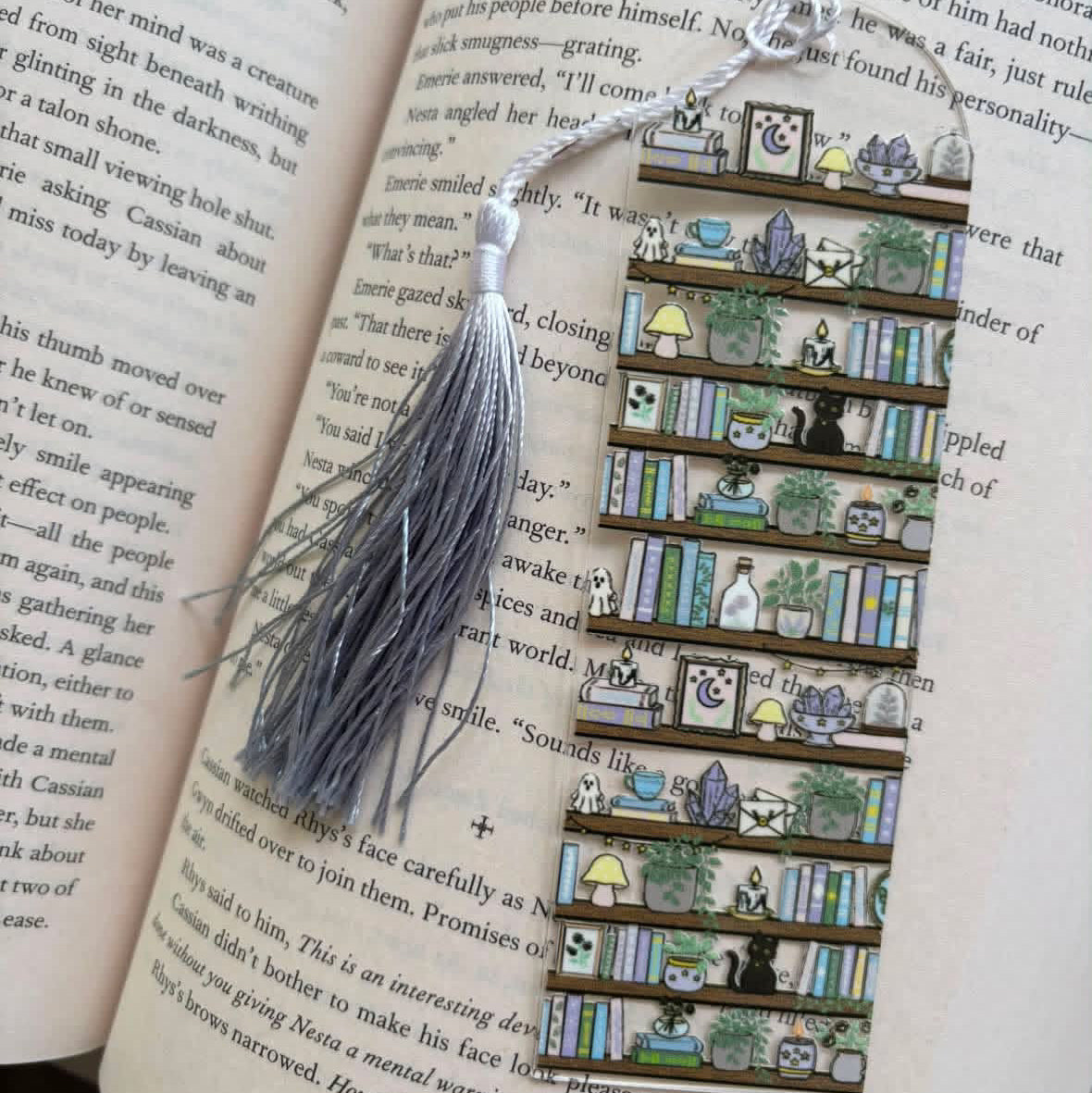 A decorative bookmark made of multiple small illustrated book spines arranged vertically, with a gray tassel and silver string, placed on an open book page.